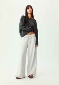 Grauer übergroßer Pullover mit weiten Ärmeln, kombiniert mit hellgrauen Jogginghosen mit elastischem Bund. Braune Plateausandalen.