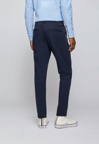 Marinblå chinos med slim fit, jämn textur, bakfickor och en subtil lyster, matchade med vita sneakers med färgglada ränder.