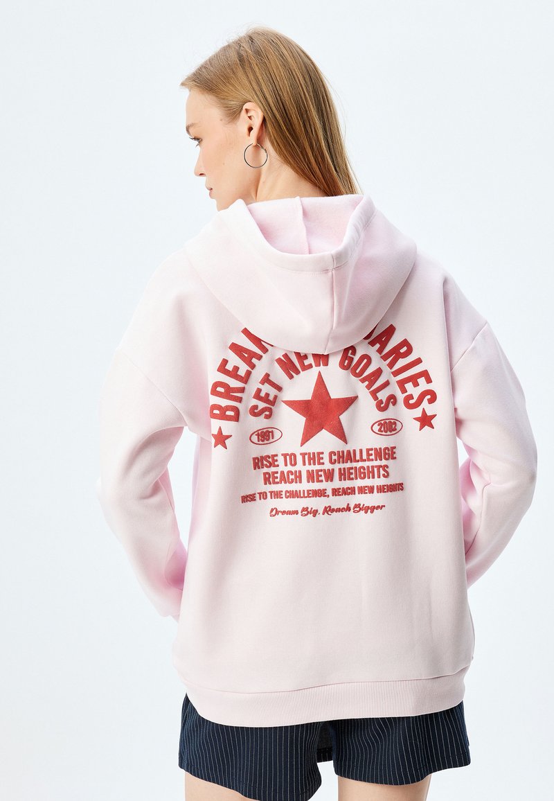 Sudadera rosa con capucha, que presenta un texto gráfico rojo y un diseño de estrella en la parte trasera. Material de mezcla de algodón; corte holgado, puños y dobladillo de canalé.