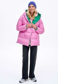 Růžová zateplená bunda se zelenou kapucí, s patentními zapínáními, obdélníkovým střihem a lesklou texturou. Vhodná k tmavým džínům a teniskám.