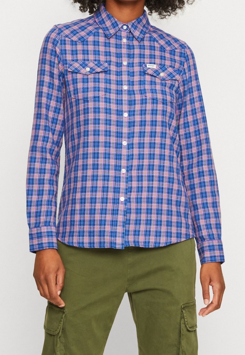 Chemise à manches longues bleue et rose à carreaux avec col, deux poches poitrine et fermeture à boutons. Tissu en coton avec une texture lisse.