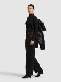 Zwart coltruitje gecombineerd met een zwarte, hooggesneden spijkerbroek en enkellaarsjes met hak. Over één schouder wordt een zwarte gewatteerde jas gedragen.