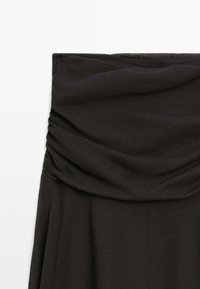 Schwarzes trägerloses Kleidungsstück mit gerafftem oberen Bereich und glattem Stoff darunter, auf weißem Hintergrund dargestellt.
