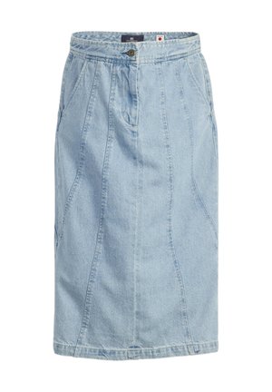 Frau trägt eine hellblaue Jeansjacke und einen dazu passenden langen Jeansrock mit schwarzen Stiefeletten mit Absatz, stehend vor einem schlichten grauen Hintergrund.
