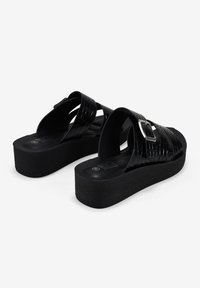 Sandalias de plataforma negras hechas de material sintético brillante con un diseño trenzado, correas anchas y un acento de hebilla cuadrada. Suela texturizada.
