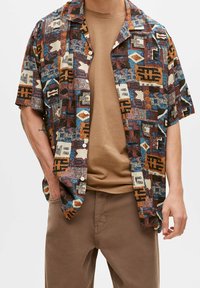 Chemise à manches courtes à motifs avec des dessins géométriques multicolores en nuances de brun, bleu et crème ; tissu léger avec une coupe décontractée.