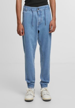 Pantalones jogger de denim azul claro con puños elásticos, cintura con cordón y bolsillos laterales. Material visible con detalles de costura de jeans normales.