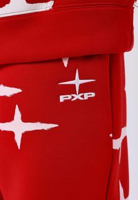 Rode joggingbroek met een gedurfde witte sterrenpatroon en een geborduurd "PXP" logo op de stof, die een gladde, zachte textuur benadrukt.