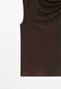 Haut sans manches marron foncé avec un col drapé, posé à plat sur une surface blanche.