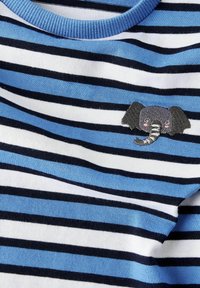 Randig t-shirt med blå, vit och marinblå mönster. Har en grå elefantbroderi på framsidan. Mjuk bomullsmaterial.