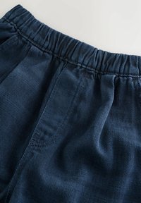 Tessuto blu a coste con un elastico in vita. La texture appare morbida con sottili strisce verticali e dettagli arricciati.