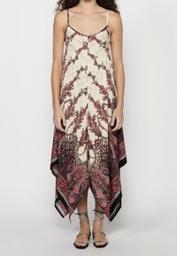 Femme portant une robe sans manches à encolure en V et ourlet en pointe, ornée de motifs floraux cachemire rouges et noirs, associée à des sandales noires à brides.