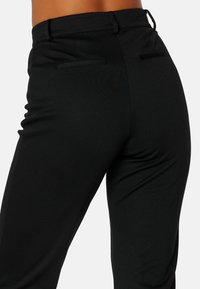 Černé kalhoty s dobře padnoucím střihem a hladkým povrchem, které mají dvě zadní kapsy a jsou vyrobeny z elastické, prodyšné látky.