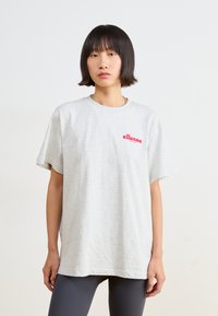 Světle šedé bavlněné tričko s krátkým rukávem. Na levé části hrudi má červené logo "ellesse". Volný střih s kulatým výstřihem.