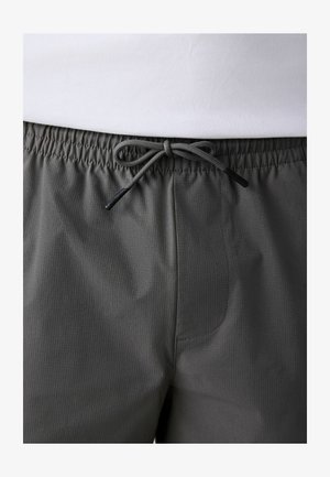 Bund einer dunkelgrauen Hose mit einem gebundenen Kordelzug und feiner vertikaler Struktur, kombiniert mit einem weißen, hineinsteckten Hemd.