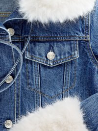 Casaco de ganga com tecido azul claro, botões prateados, gola de pelúcia sintética e costuras à vista. Apresenta um bolso frontal e superfície texturizada.