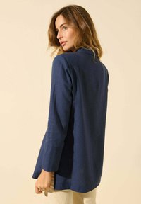 Haut à manches longues bleu marine en tissu lisse avec une coupe décontractée, doté d'un col arrondi et d'entailles sur les côtés pour faciliter les mouvements.