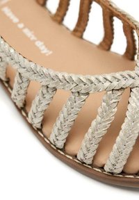 Sandalo intrecciato con cinturini intrecciati argentati e suola beige. Tessuto morbido con un design aperto sulla punta e suola piatta. Dettagli di cucitura semplici.