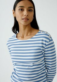 Blau-weiß gestreiftes Langarmoberteil mit weitem Ausschnitt, ausgestattet mit vier dekorativen Knöpfen an der linken Schulter. Weich, strukturiertes Material.