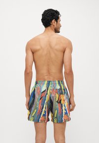 Maillots de bain colorés avec un motif tropical, taille élastique et une poche arrière. Fabriqués en tissu léger avec un design éclatant.