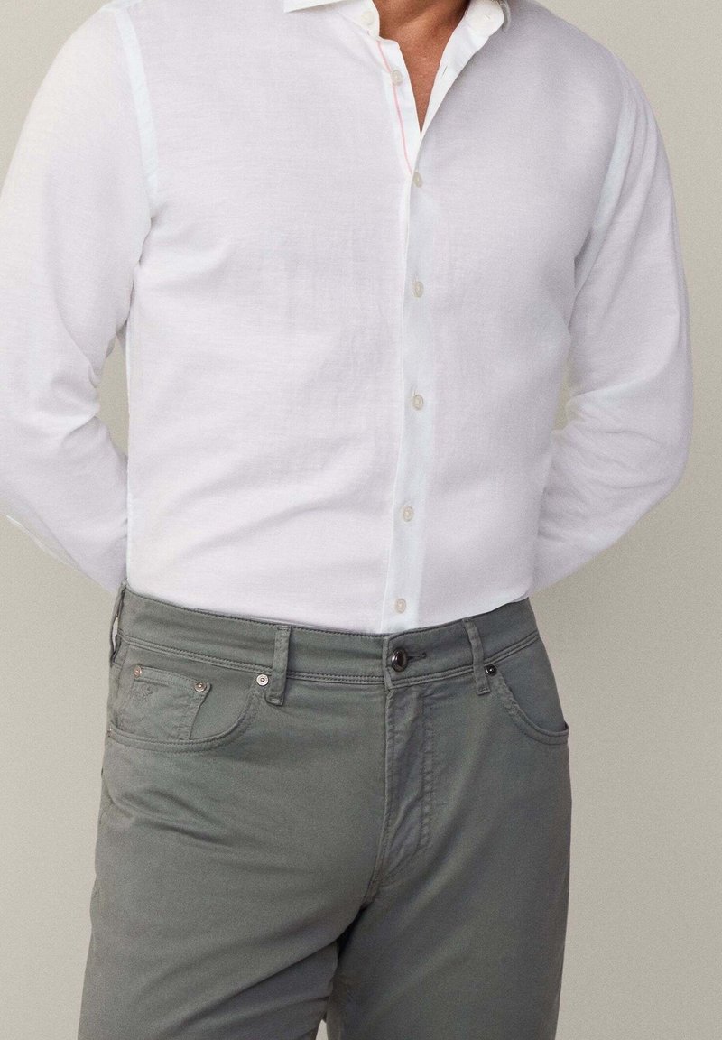 Witte linnen blouse met een button-down kraag, gecombineerd met grijze katoenen broek met een knoop en voorkeurszakken.