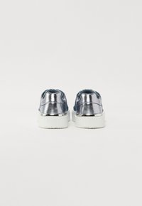 Μεταλλικό ασημί αθλητικό παπούτσι με λευκή καουτσούκ σόλα, υφασμάτινη υφή και στρογγυλή μορφή. Διαθέτει λογότυπο στη φτέρνα και μίνιμαλ σχέδιο.