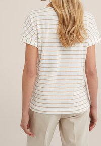 Randig kortärmad t-shirt i vitt med beige horisontella linjer, med en rund halsringning och uppvikt ärmslut, bärs med ljusa byxor.