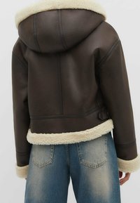 Veste cropped en cuir marron avec une capuche en shearling crème, des poignets et un ourlet. Présente des détails de couture et une coupe décontractée.
