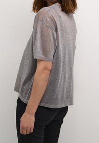 Top a maniche corte in tessuto metallico argento con una texture trasparente. Vestibilità ampia, scollo rotondo, superficie leggermente lucida. Abbinabile con pantaloni scuri.