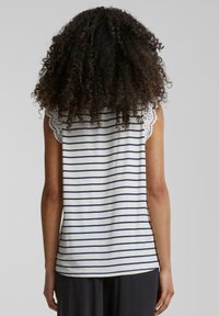 Haut sans manches rayé en blanc avec des lignes navy, présentant des accents en dentelle aux épaules. Texture de coton lisse, coupe décontractée.