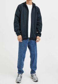 Laivasto sininen huppari pehmeästä kankaasta, päällä valkoinen paita, yhdistettynä sinisiin farkkuihin ja harmaisiin tennareihin.