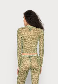 Top de mangas longas, ajustado, e leggings combinando em tecido de malha semi-transparente. Padrão geométrico verde, com bordas em contraste.