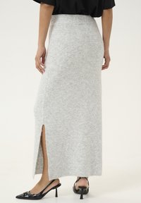 Jupe maxi grise en tricot avec une fente latérale, ceinture côtelée et finition texturée. Portée avec des escarpins noirs à bout pointu.