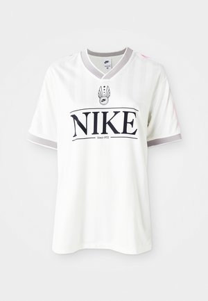 Valkoinen Nike-t-paita lyhyillä hihoilla, jossa on pystysuoria raitoja, harmaa kaulus ja suuri musta logo, jossa on teksti "Since 1972."