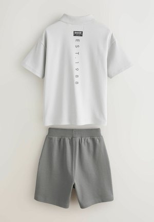 Helehall mõrkjal polo-pluus lühikeste varrukate ja kraega, millel on must silt ja hall trükitud tekst. Sellega kaasnevad hallid lühikesed püksid elastse vöökohaga.