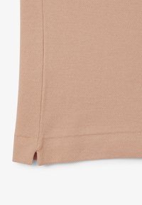 Tela de punto de color rosa claro con una superficie texturada. Presenta una abertura lateral en el dobladillo y un borde limpio y acabado.