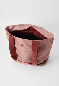 Bolsa tote de nylon rosa con asas rojas, que cuenta con un interior espacioso y un bolsillo de malla. Pequeño detalle de logo en un lado.
