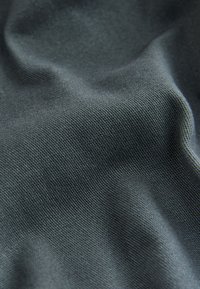 Tissu gris foncé avec une texture fine en maille et des plis doux créant des ombres et des reflets délicats.