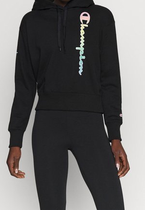 Sudadera negra corta hecha de tela suave. Presenta un colorido logo de "Champion" en la parte delantera, capucha con cordón y puños acanalados.