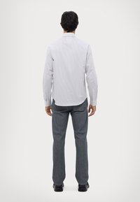 Camisa de manga larga blanca a rayas con puños de botón, combinada con jeans grises. La camisa presenta un collar clásico y un dobladillo curvado.