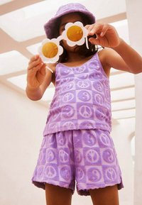 Lila, texturerad tank top och shorts-set med mönster av fredstecken. Accessoarer i form av vita solglasögon i blommig form med gula linser.