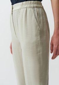 Pantaloni beige chiaro realizzati in un tessuto leggero e morbido, con vita elastica e tasche laterali. Superficie testurizzata con una vestibilità comoda.
