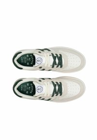 Zapatillas con parte superior de cuero y ante color crema, acentos verde oscuro, puntera perforada, cordones verdes y un logo circular en la lengüeta.