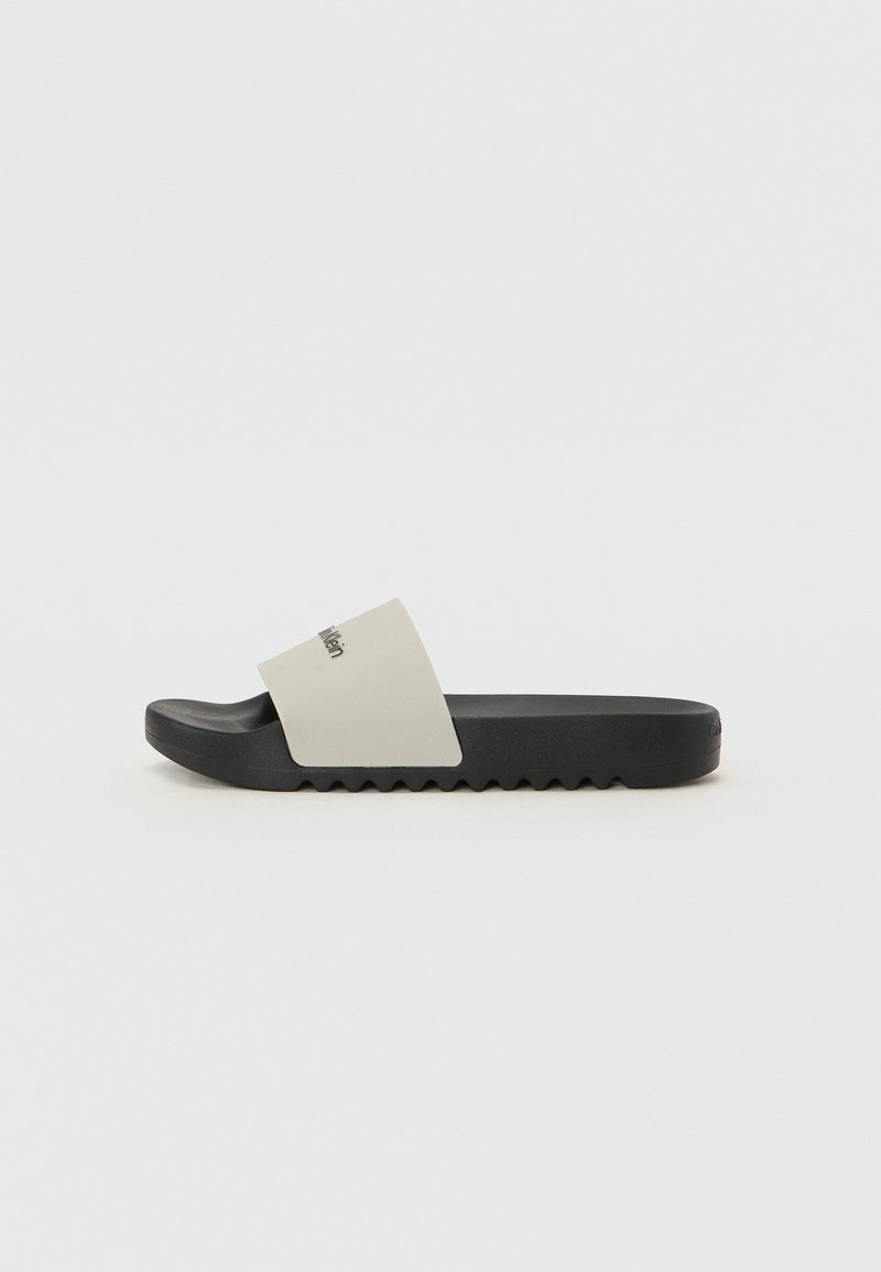 Sandală tip slide cu talpă mată neagră și o bandă lată, netedă, de culoare gri, cu un logo. Fundă texturată pentru aderență. Design simplu și plat.