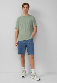 Jasnozielona bawełniana koszulka w połączeniu z niebieskimi szortami dżinsowymi. Stylizację dopełniają szare i białe trampki oraz paskowane skarpetki.