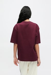 Bordó színű, bő fazonú rövid ujjú póló, kerek nyakkivágással, puha pamutból, hátulról bemutatva.
