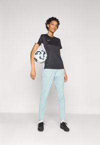 Black and white short-sleeve athletic shirt with a logo, paired with light blue tapered pants featuring pink accents. Holding a soccer ball.