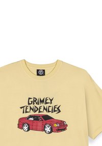 Camiseta de algodón amarilla con un gráfico de un coche rojo y el texto "GRIMEY TENDENCIES" en negrita negra. Mangas cortas y cuello redondo.