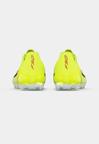 Ελαφριά ποδοσφαιρικά παπούτσια σε φωτεινό κίτρινο με κόκκινες πινελιές, με κομψό σχεδιασμό, υφή στην επιφάνεια και διαφανές πέλμα.