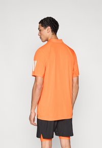 Polo de manga corta en color naranja brillante, diseñado con cuello y detalle de logotipo en la manga izquierda. Material sintético liso y ligero.